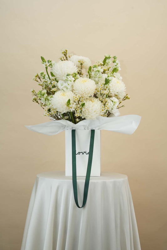 White chrysanthemums and filler flowers in white Flovia flower bag with green handle - Dubai